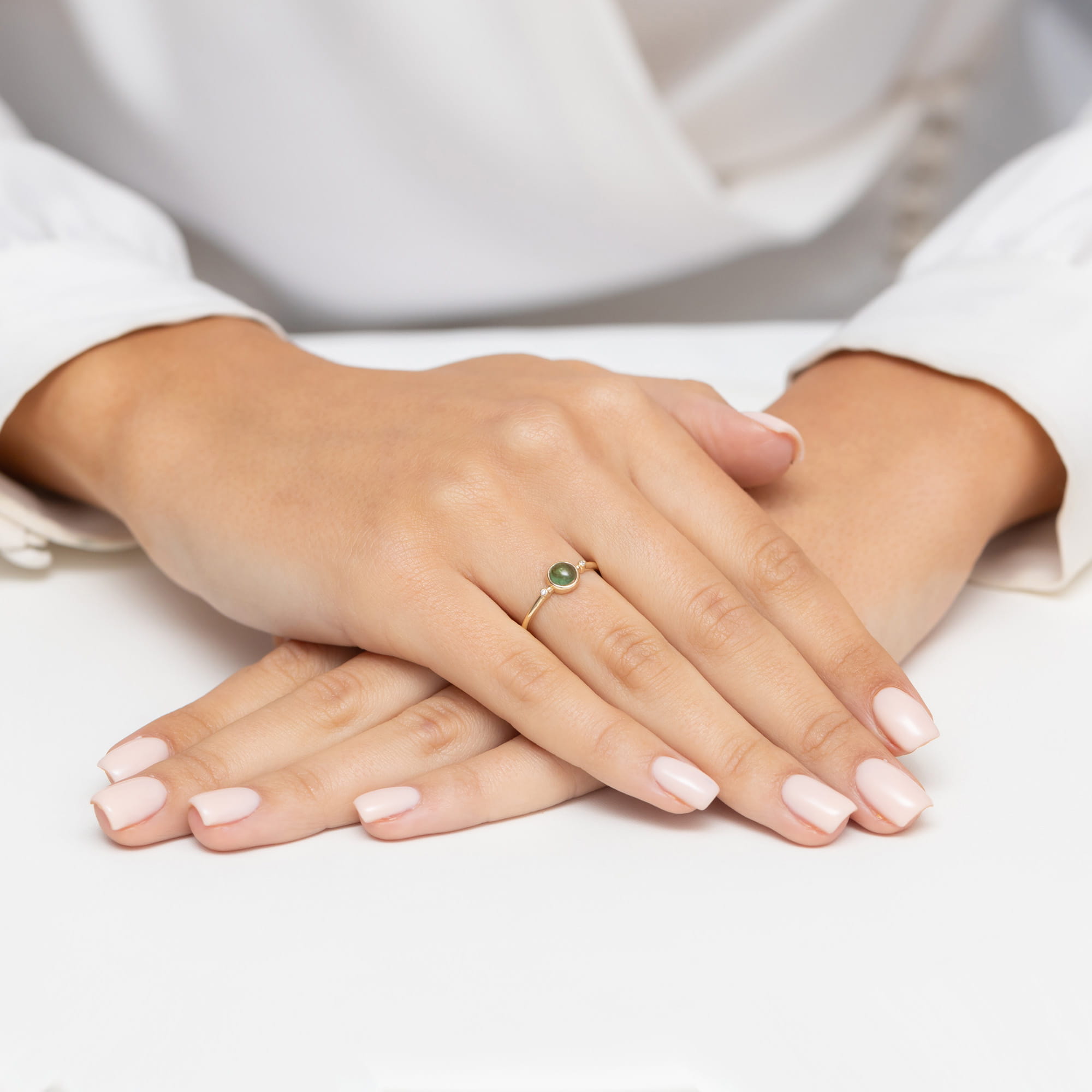W0597.Z3.TMG.01_4 Dwie ręce z delikatnym pierścionkiem i różowym manicure, ułożone na białym tle.