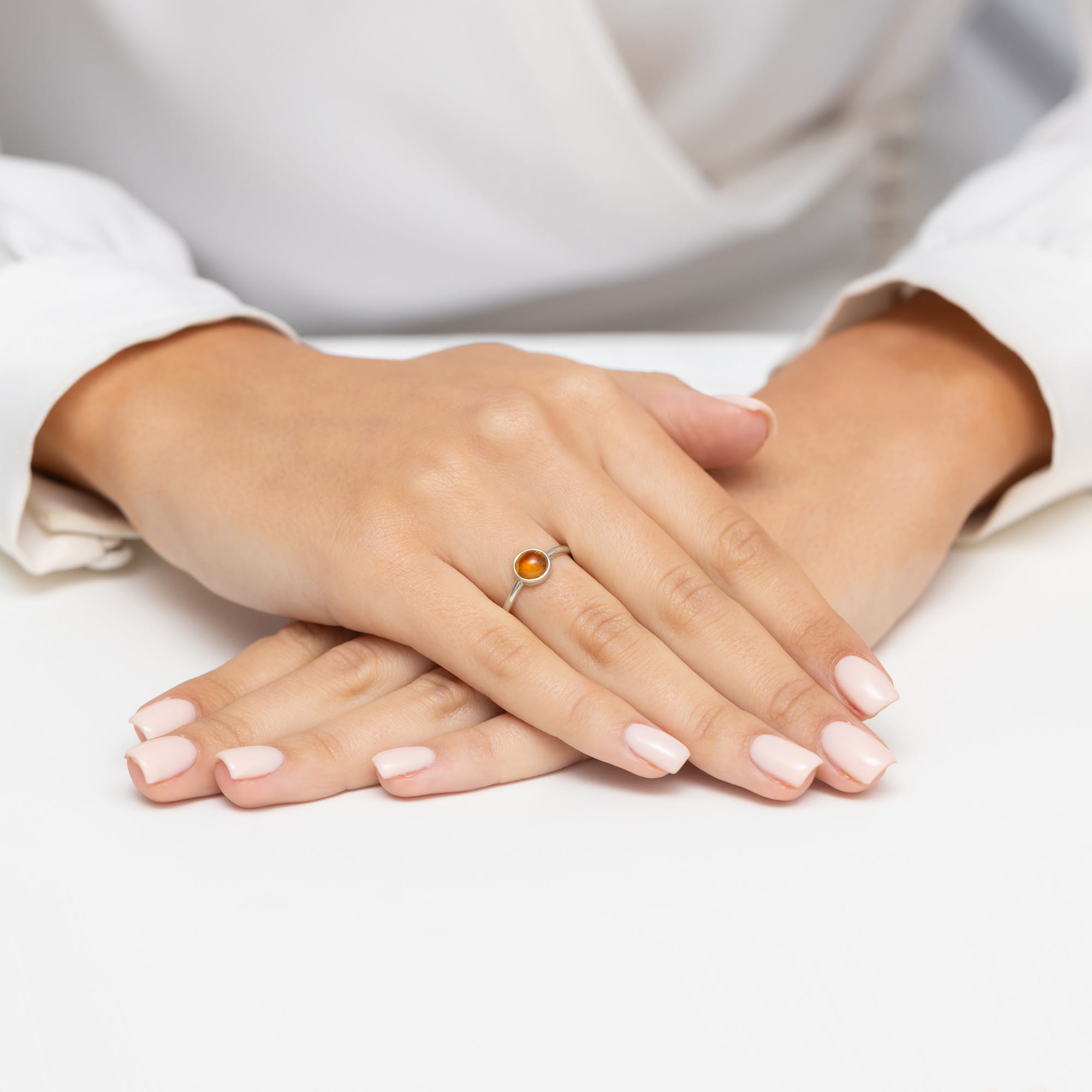 W0598.B3.TMY.01_4 Na dłoniach z delikatnym manicure znajduje się srebrny pierścionek z pomarańczowym kamieniem.
