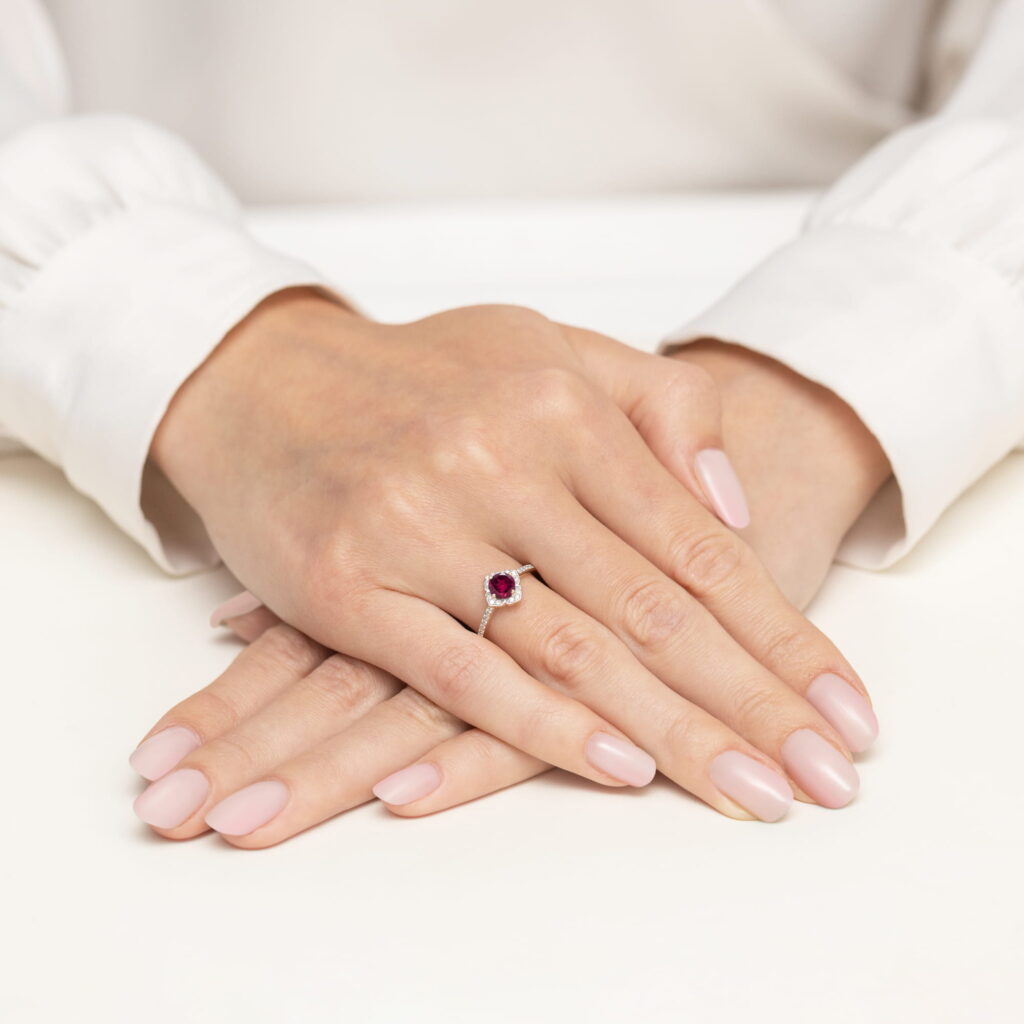 Na dłoni z delikatnym manicure znajduje się pierścionek z czerwonym kamieniem szlachetnym.