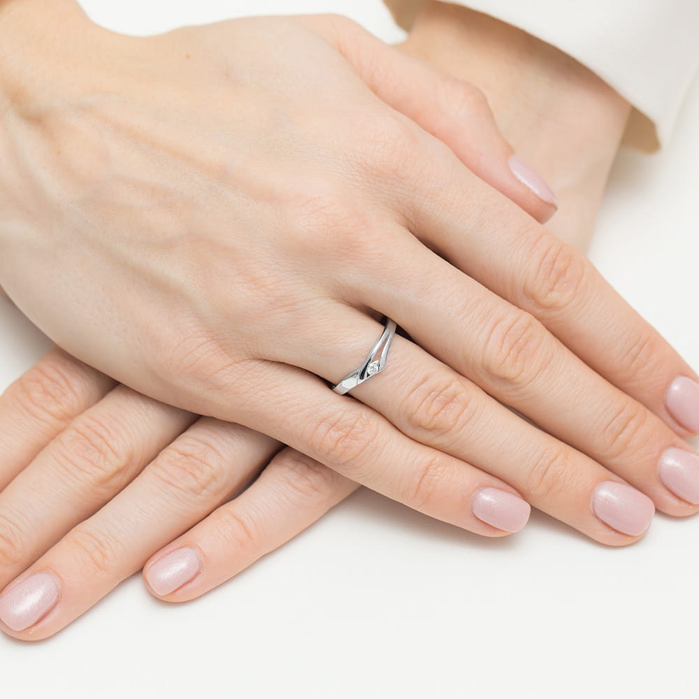 W0609.B3.DIW.01_4 Dwie ręce z delikatnym pierścionkiem na palcu, paznokcie w jasnym kolorze, skórzana powierzchnia.