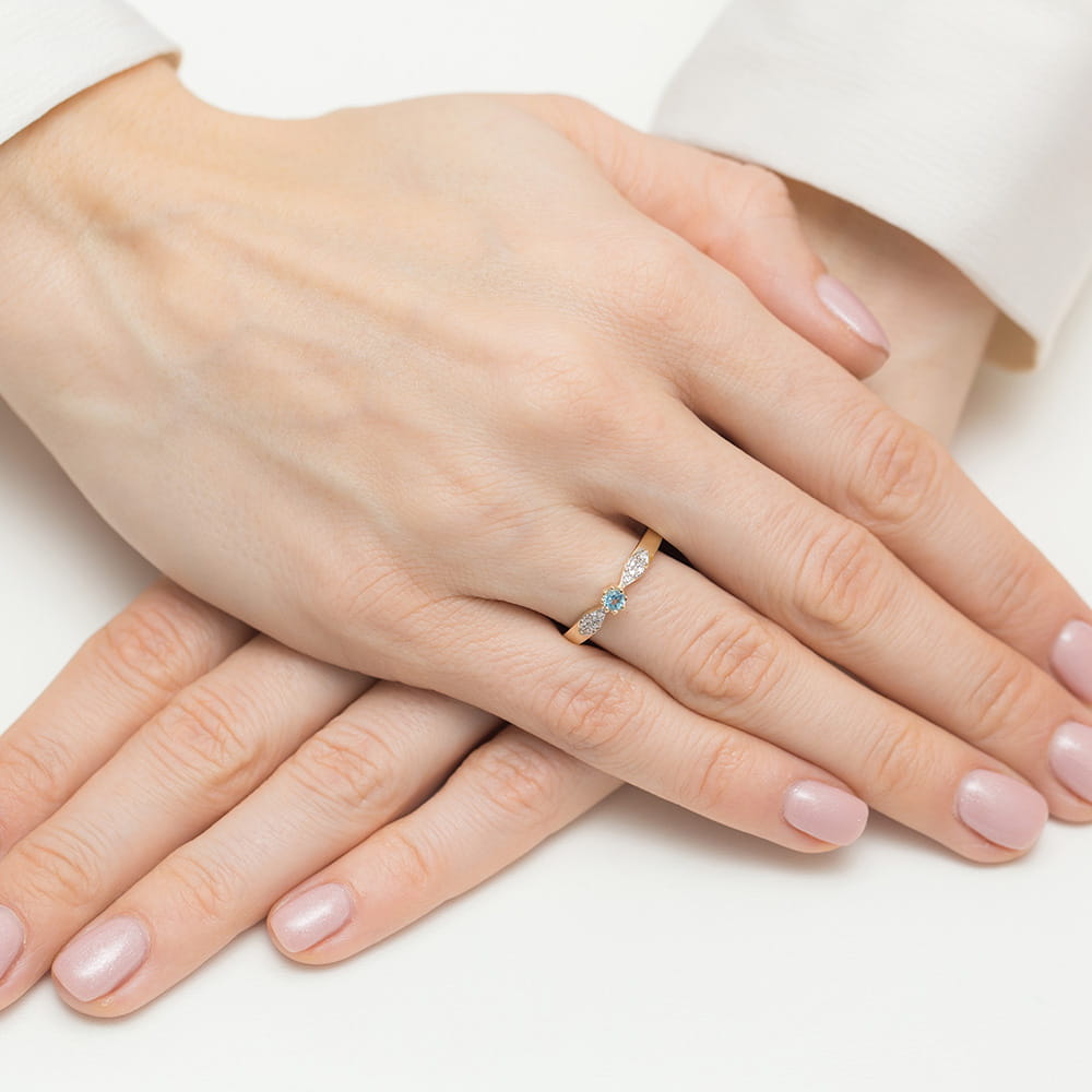 W0613.B3.TOB.01_4 Dwie dłonie z delikatnym pierścionkiem na palcu, z subtelnymi kamieniami w kolorze niebieskim.