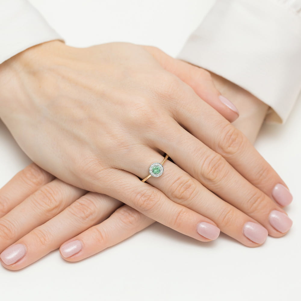 W0616.Z3.EMG.01_4 Dwie dłonie z delikatnym pierścionkiem z zielonym kamieniem na palcu, paznokcie w jasnym kolorze.