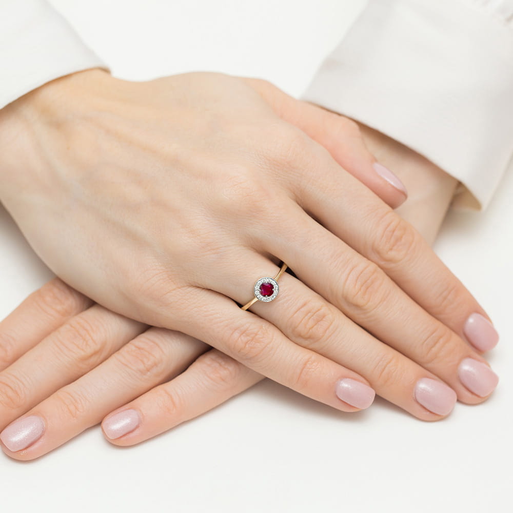 W0616.Z3.RUR.01_4 Na dłoniach z delikatnym manicure znajduje się złoty pierścionek z czerwonym kamieniem w centralnej części.