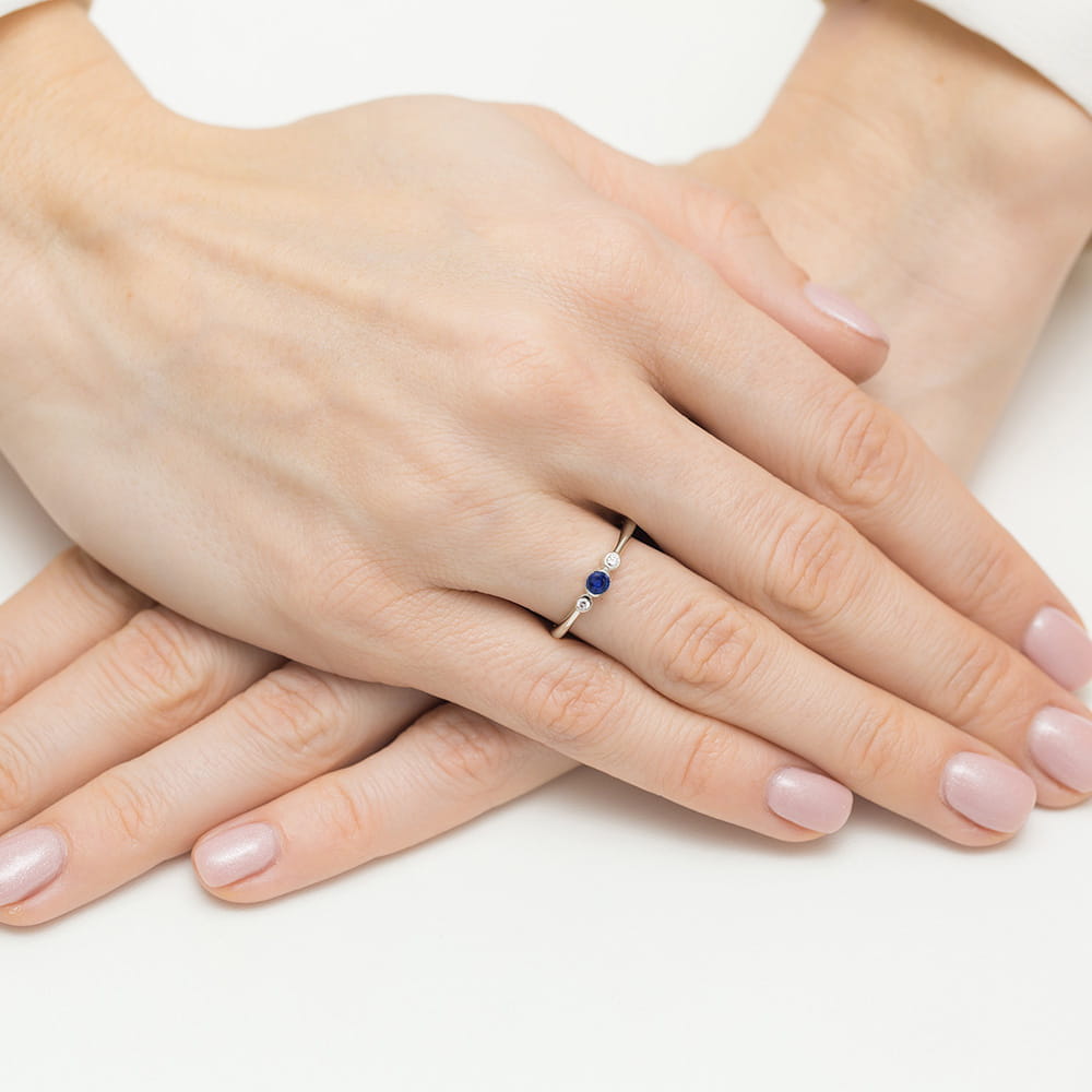 W0620.B3.SAB.01_4 Dwie dłonie z delikatnym pierścionkiem z niebieskim kamieniem na palcu. Paznokcie w jasnym kolorze.