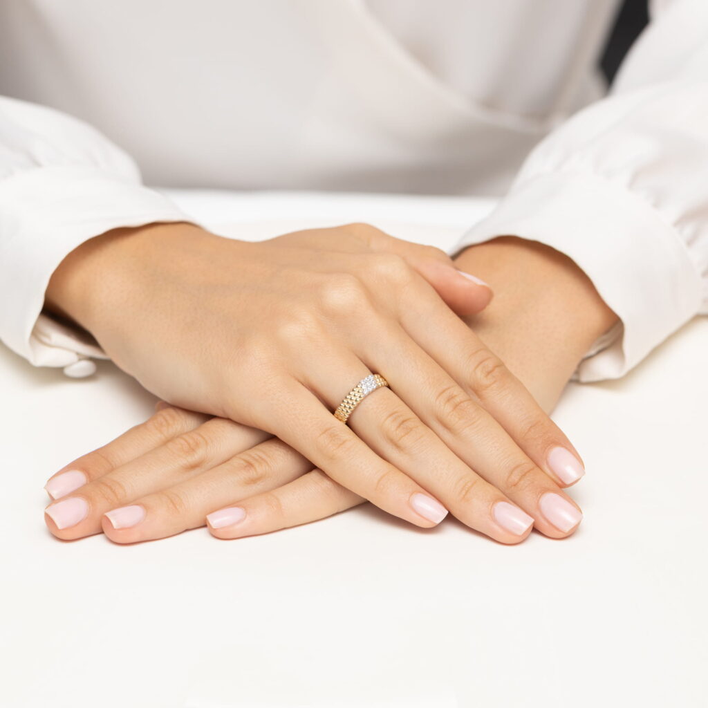 Dwie ręce z delikatnym manicurem, jedna z pierścionkiem na palcu, leżą na białym stole.