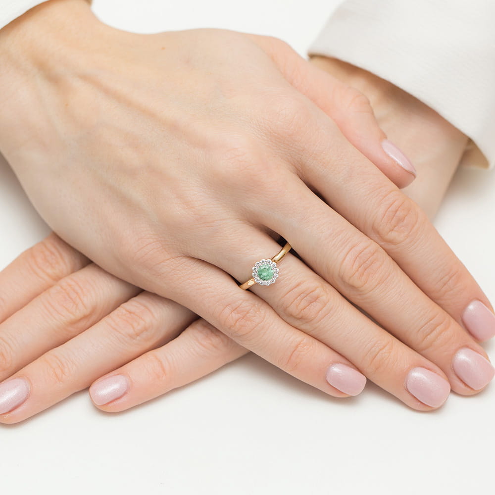 W0622.Z3.EMG.01_4 Złoty pierścionek z zielonym kamieniem i diamentowym otoczeniem na dłoni z delikatnym manicure.