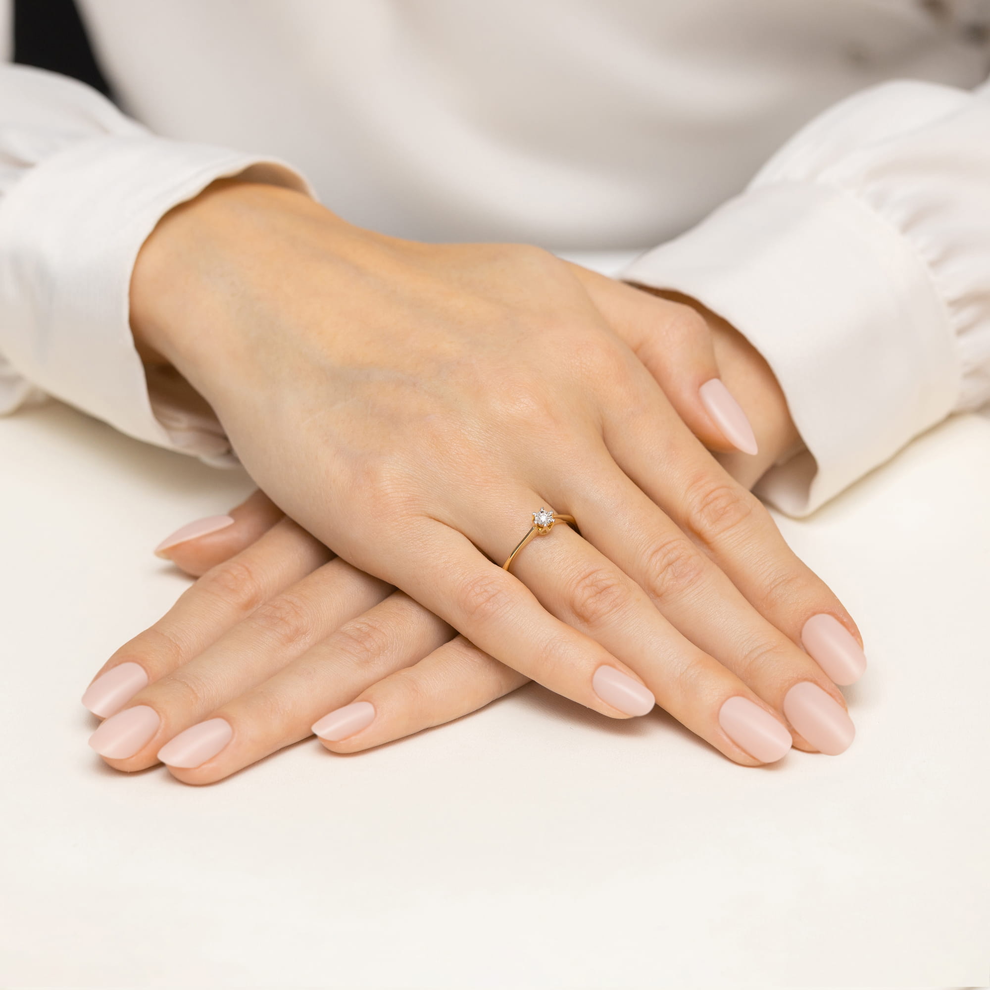 W0628.Z3.DIW.01_4 Dwie dłonie z delikatnym manicure w odcieniu nude, jedna z pierścionkiem na palcu serdecznym.