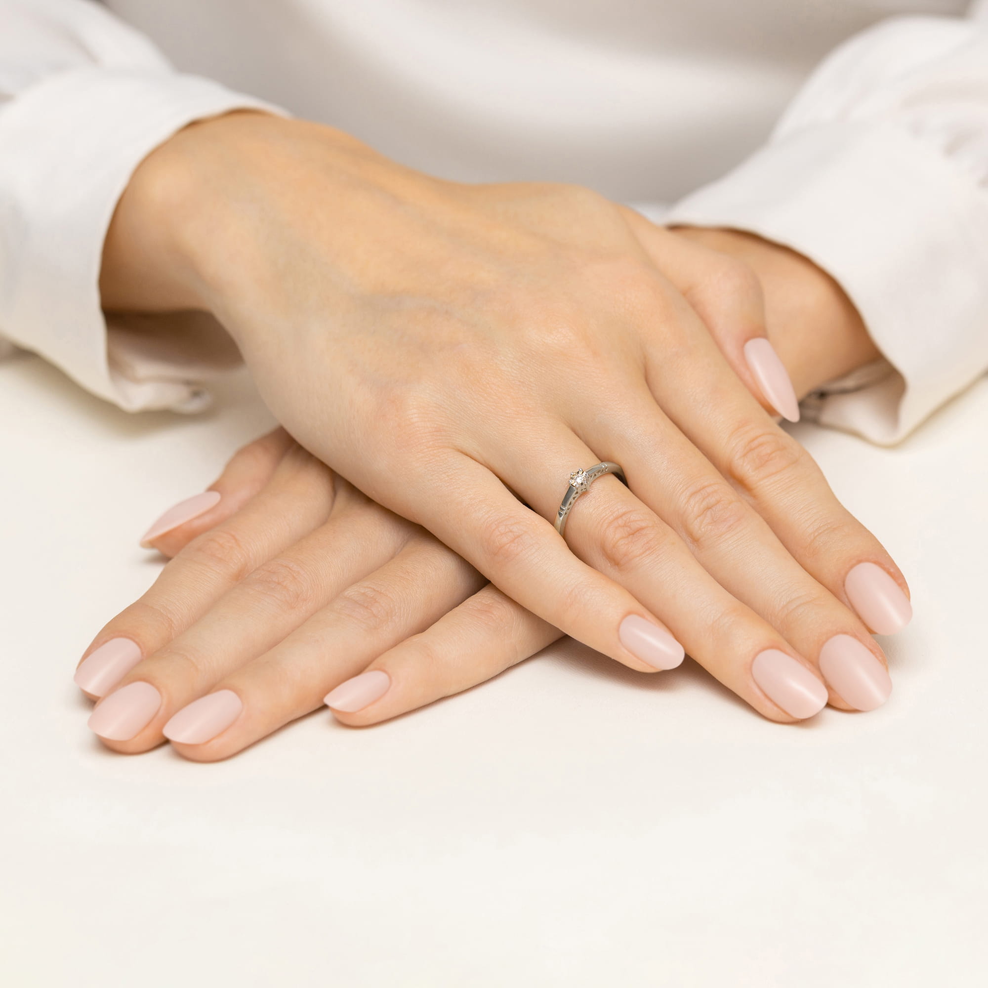 W0630.B3.DIW.01_4 Dwie ręce z delikatnym manicure w odcieniu nude, jedna z pierścionkiem na palcu serdecznym.