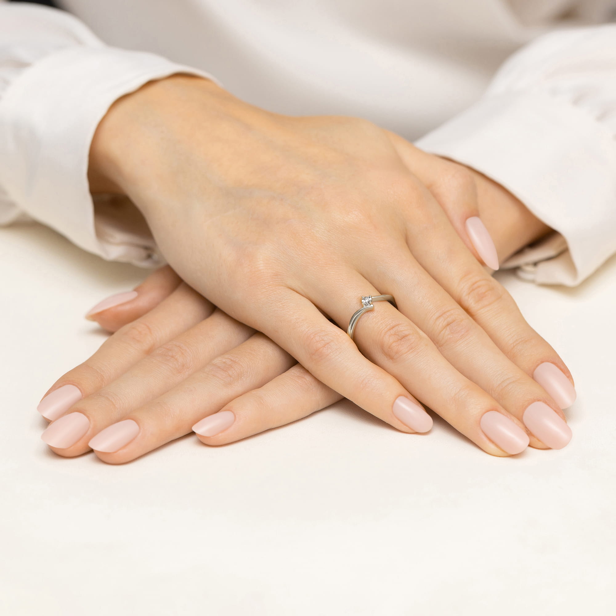 W0631.B3.DIW.01_4 Dwie dłonie z delikatnym manicure w odcieniu różowym, jedna z pierścionkiem na palcu.