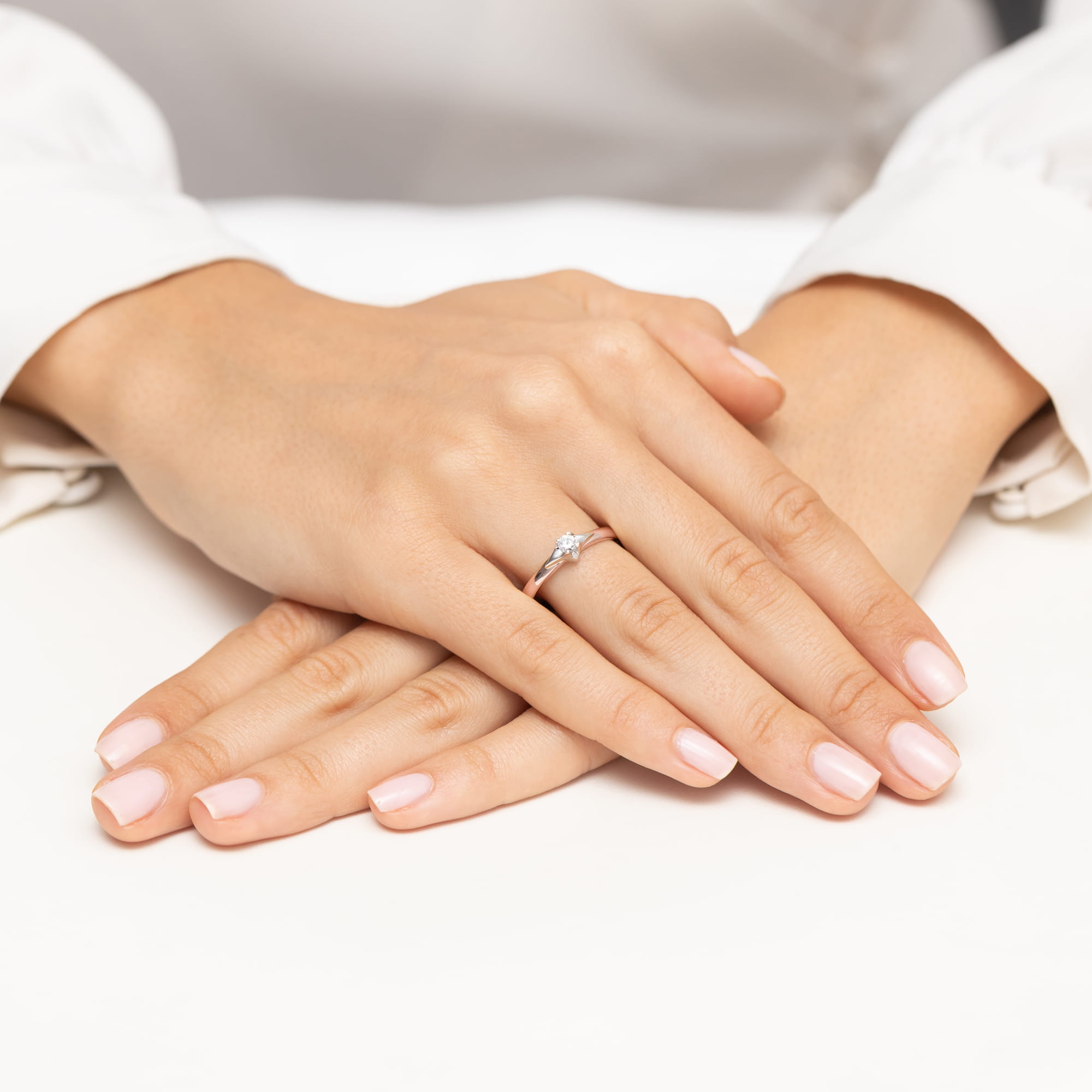 W0666.R3.DIW.01_4 Dwie dłonie z delikatnym pierścionkiem na palcu, z zadbanymi paznokciami w jasnym kolorze.