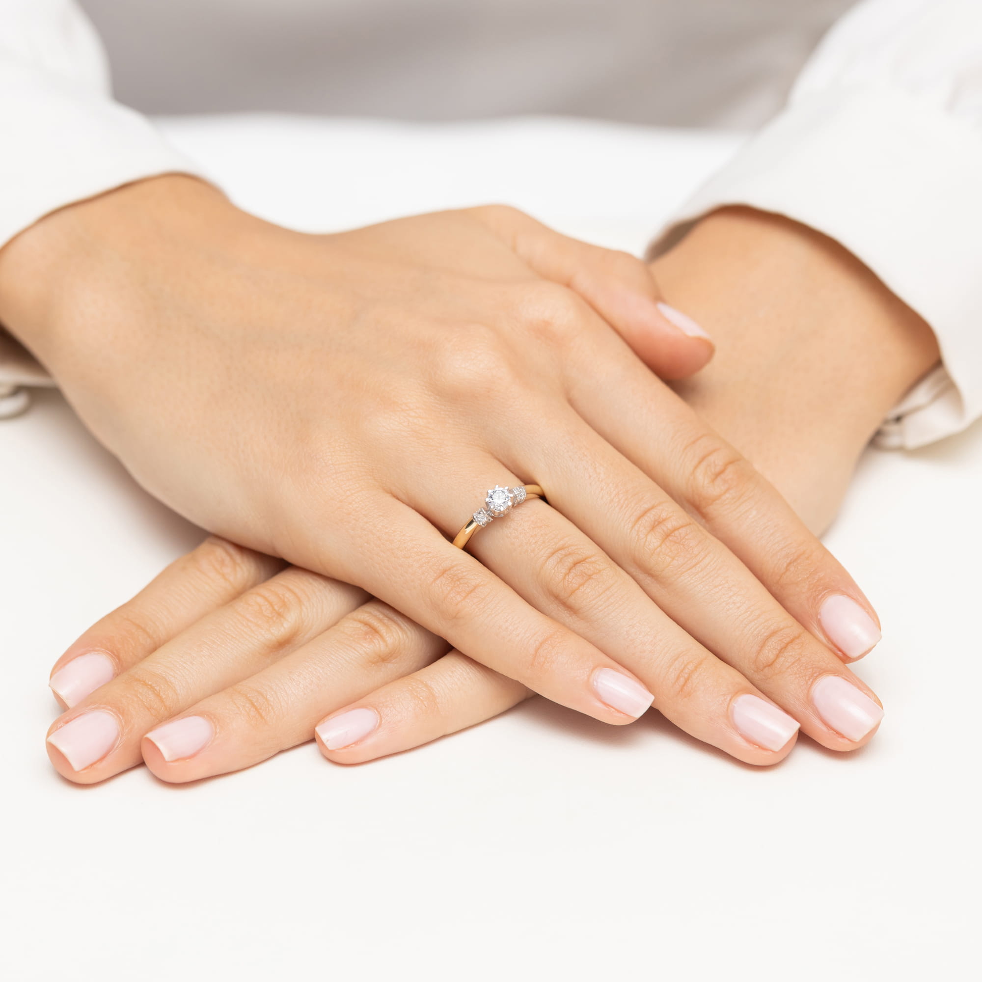 W0667.Z3.DIW.01_4 Dwie dłonie z delikatnym manicure, jedna z pierścionkiem z diamentem na złotej obrączce.