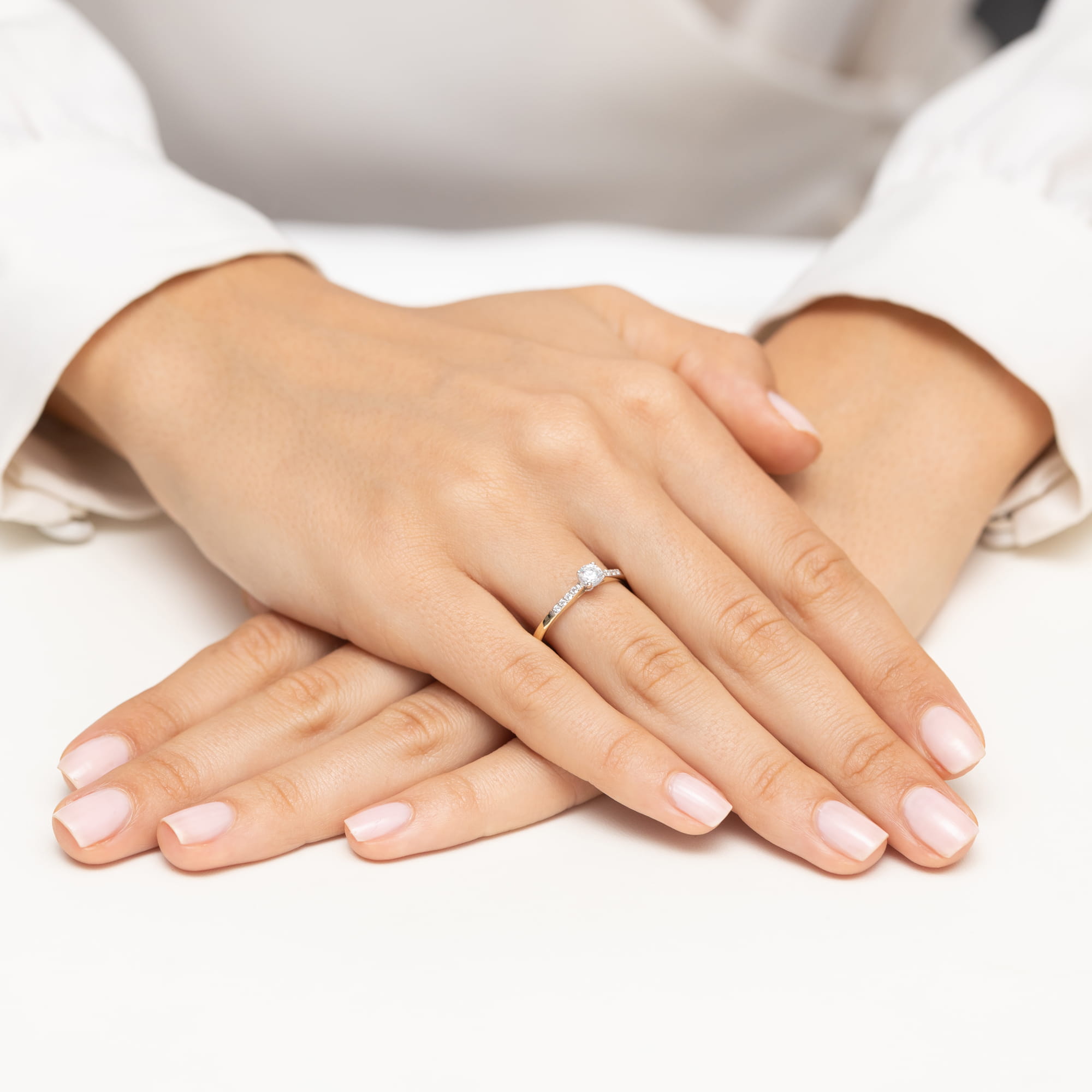 W0668.Z3.DIW.01_4 Dwie dłonie z delikatnym manicure, na jednej z nich pierścionek z diamentem.