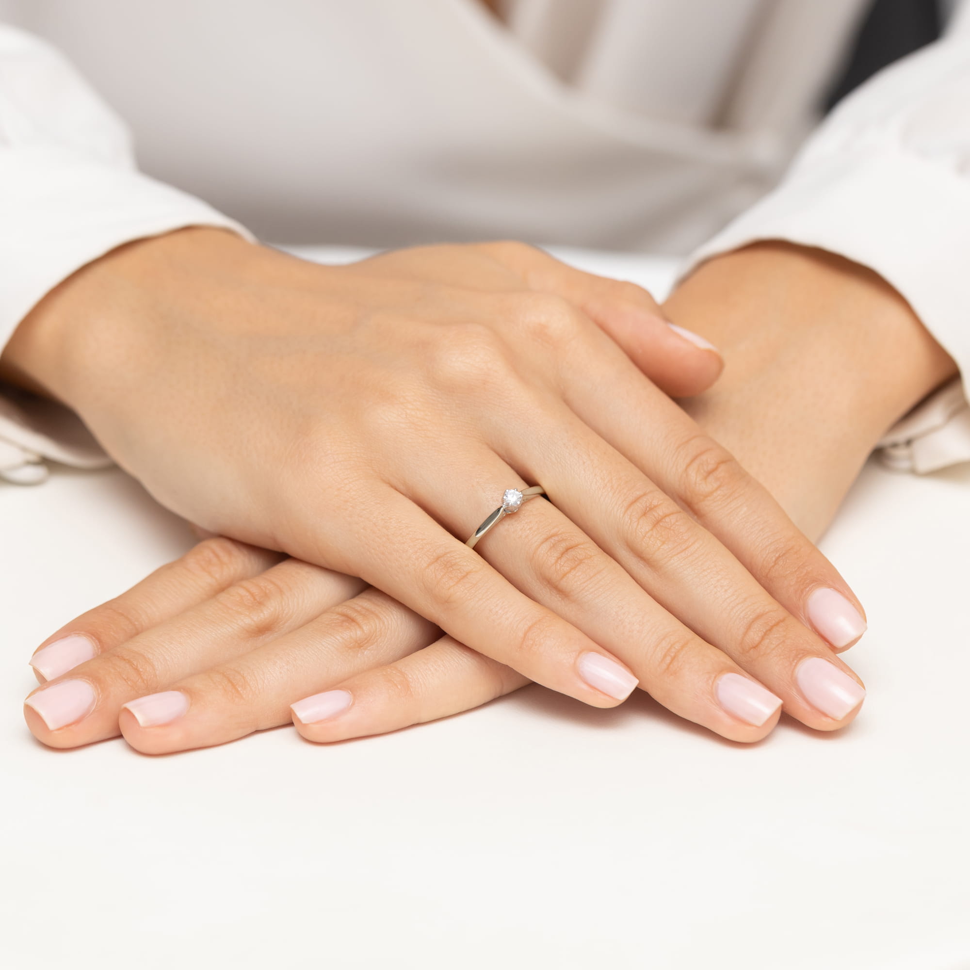 W0672.B3.DIW.01_4 Dwie ręce z delikatnym manicure, na jednej z nich srebrny pierścionek z diamentem.