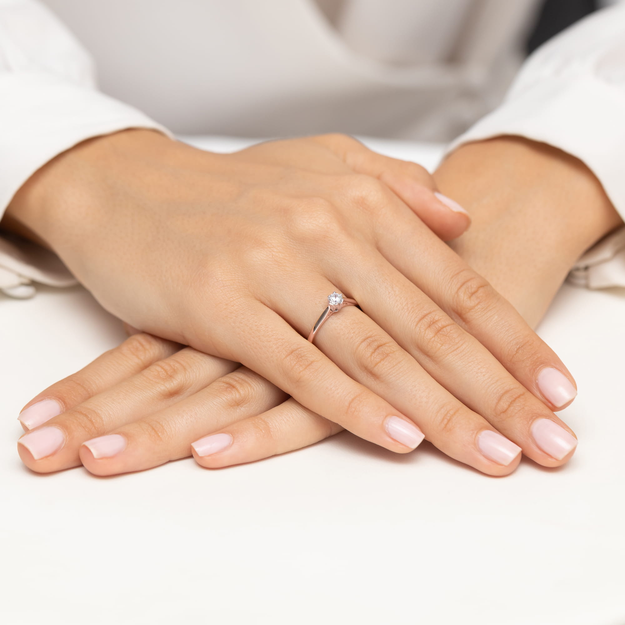 W0672.R3.DIW.02_4 Dwie ręce z delikatnym pierścionkiem na palcu, z zadbanymi, różowymi paznokciami.