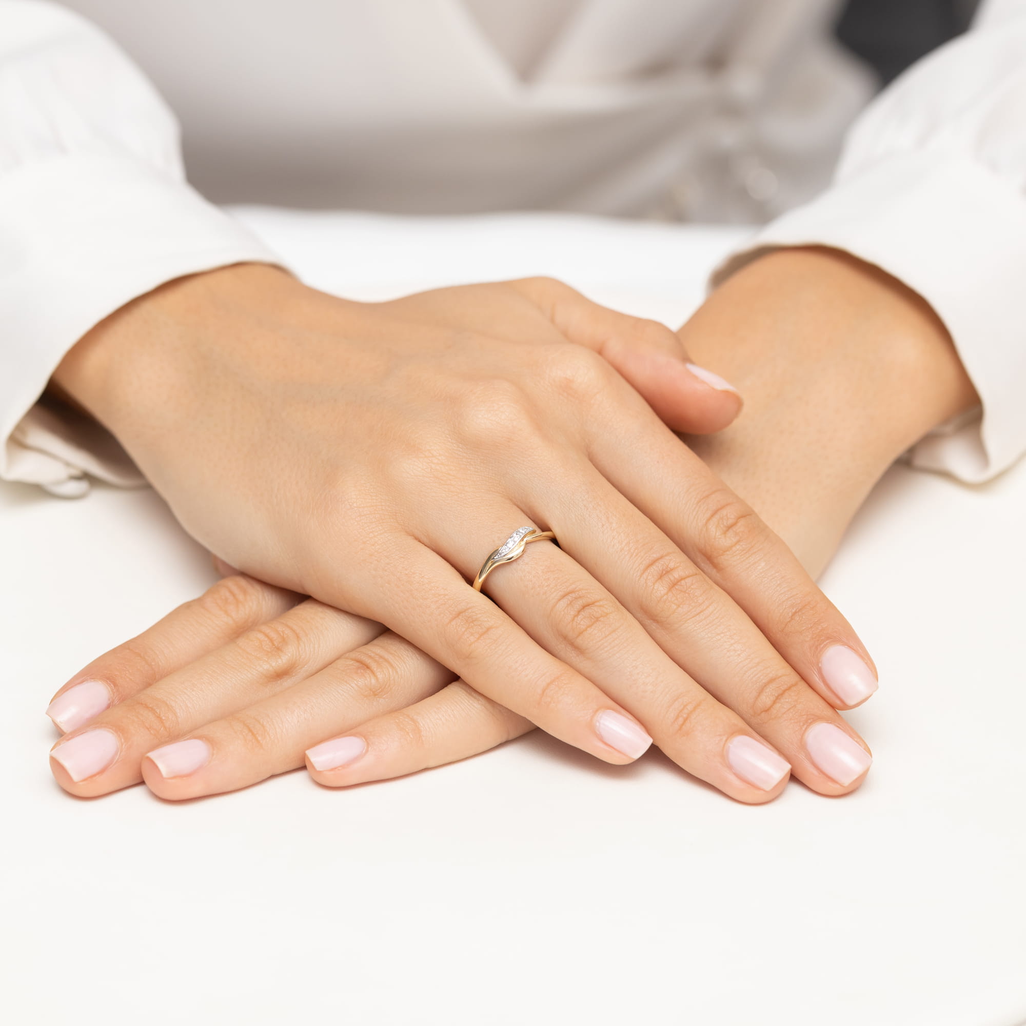 W0673.Z3.DIW.01_4 Dwie dłonie z delikatnym pierścionkiem na palcu, z zadbanymi paznokciami, leżą na białym tle.