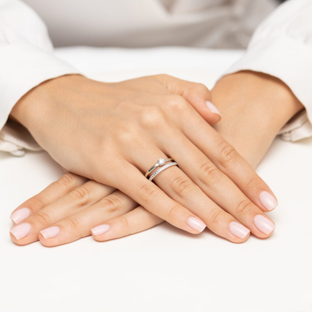 Dwie ręce z delikatnym manicure, na jednej z nich pierścionek z diamentami.