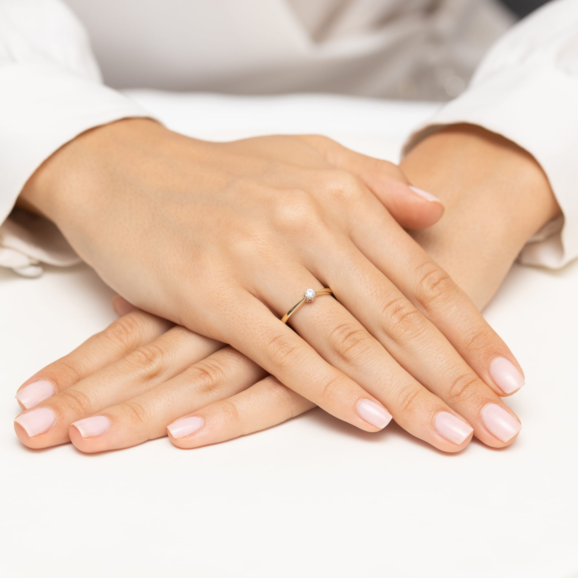 W0675.Z3.DIW.01_4 Dwie ręce z delikatnym pierścionkiem na palcu, z zadbanymi paznokciami w jasnym kolorze.