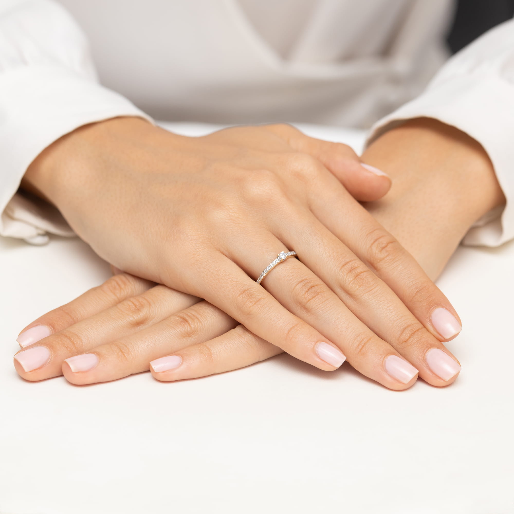 W0676.Z3.DIW.01_4 Dwie ręce z delikatnym pierścionkiem na palcu, z zadbanymi paznokciami w jasnym kolorze.