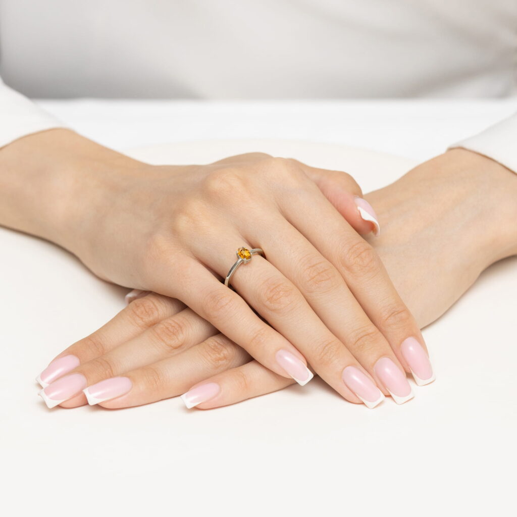 Dwie dłonie z różowym manicure i białymi końcówkami, jedna z pierścionkiem z żółtym kamieniem.