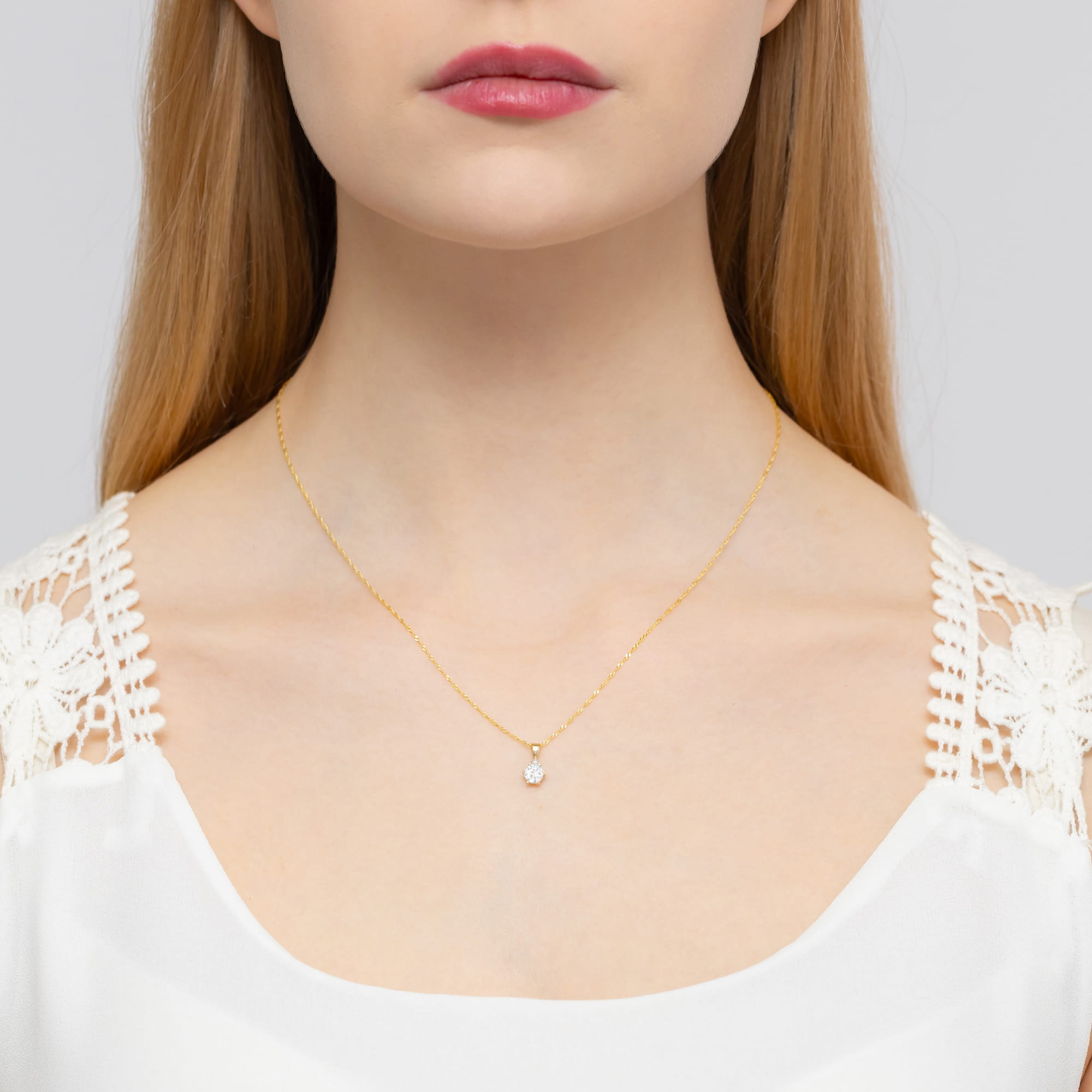 Z0076.Z3.SAW.01_2 Kobieta z długimi włosami nosi złoty naszyjnik z małym, błyszczącym kamieniem.