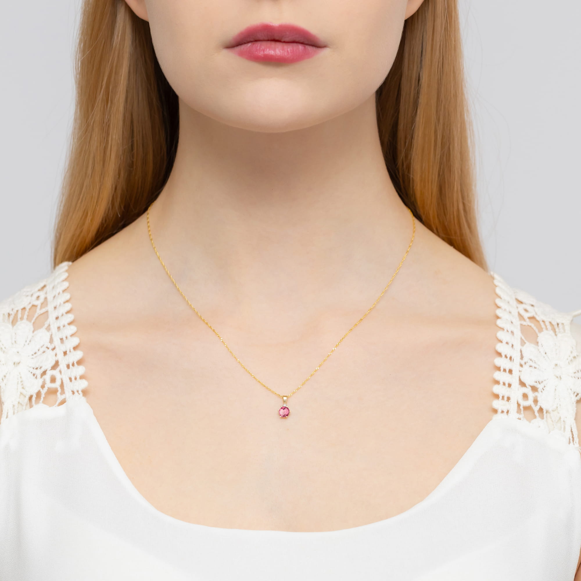 Z0076.Z3.TOP.01_2 Kobieta z długimi włosami nosi złoty naszyjnik z różowym kamieniem na delikatnym łańcuszku.
