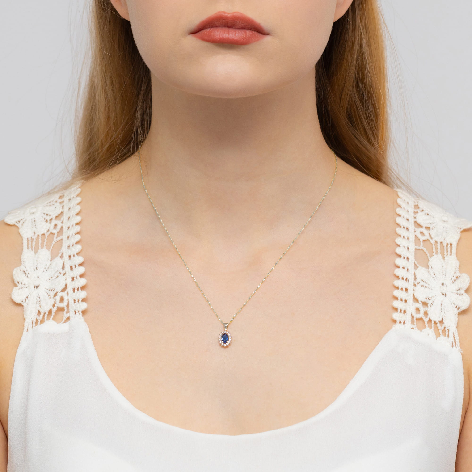 Z0182.B3.SAB.01_2 Kobieta z długimi włosami nosi delikatny naszyjnik z niebieskim kamieniem na złotym łańcuszku.