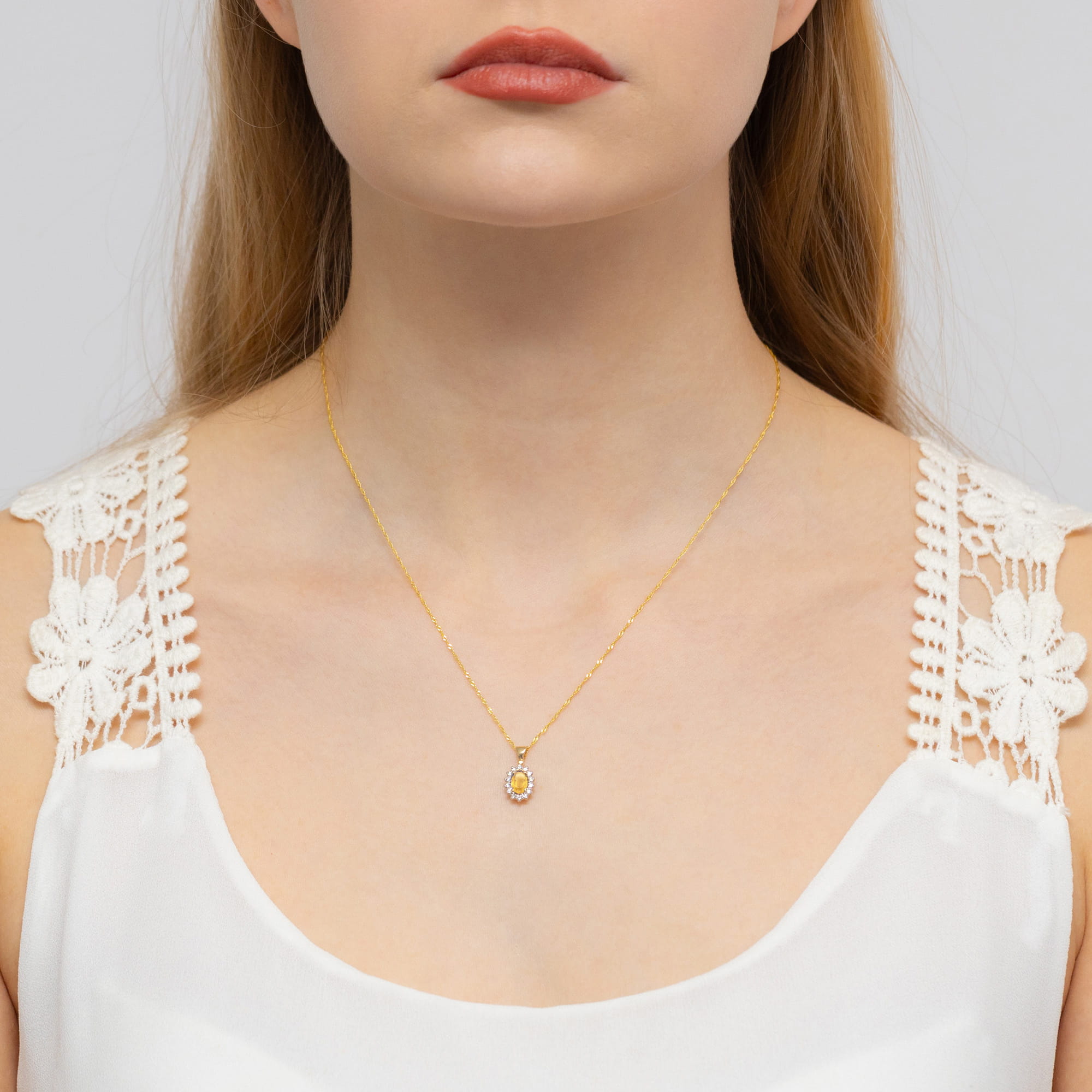 Z0182.Z3.CIY.01_2 Kobieta z długimi włosami nosi złoty naszyjnik z kolorowym wisiorkiem, ubrana w bluzkę z koronkowymi detalami.