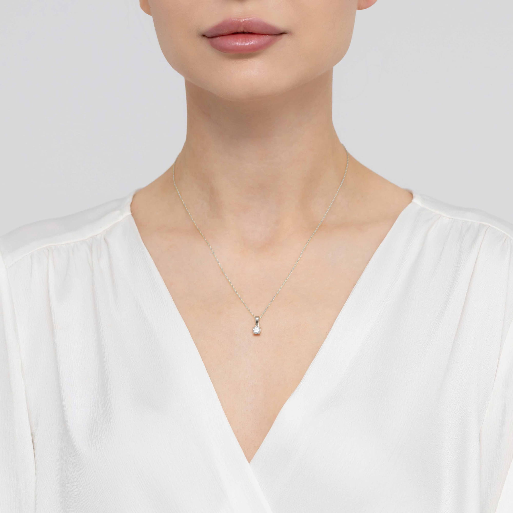 Z0576.B3.LDW.02_3 Kobieta w białej bluzce z delikatnym naszyjnikiem na szyi, z subtelnym wisiorkiem.