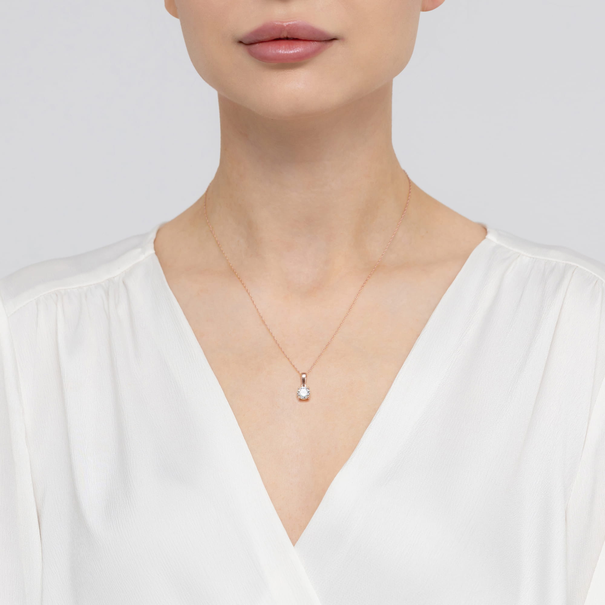 Z0576.R3.LDW.05_3 Kobieta w białej bluzce nosi delikatny naszyjnik z zawieszką w kształcie kulki.